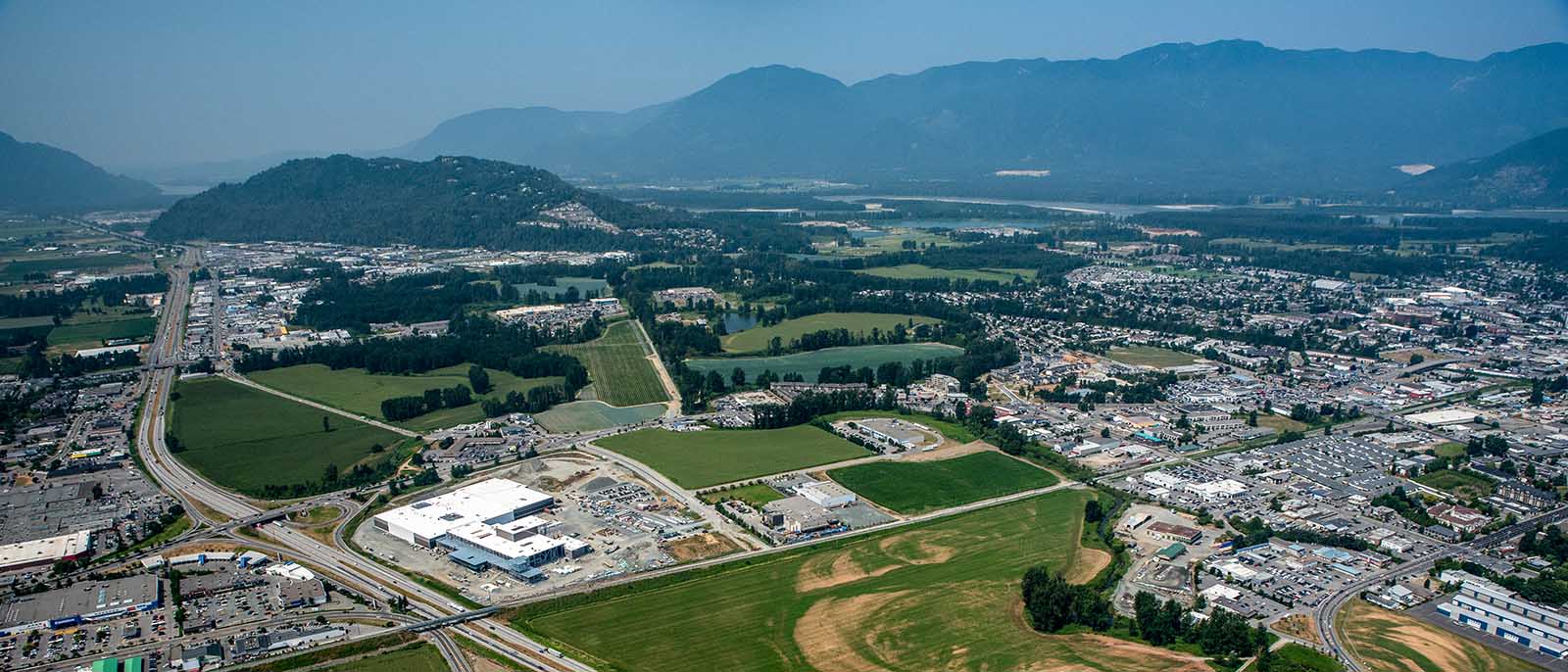 Aerial photo of Chilliwack, facing west with the airport and downtown visible on the right side of the image, Highway 1 and industrial buildings visible on the left side of the image